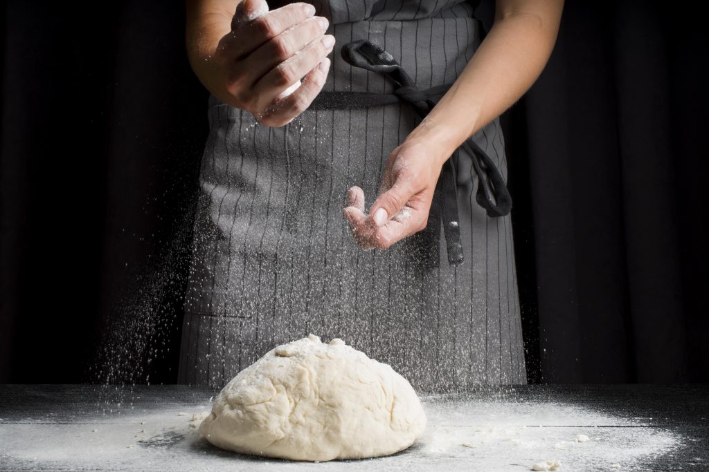 mid shot baker pouring flour dough